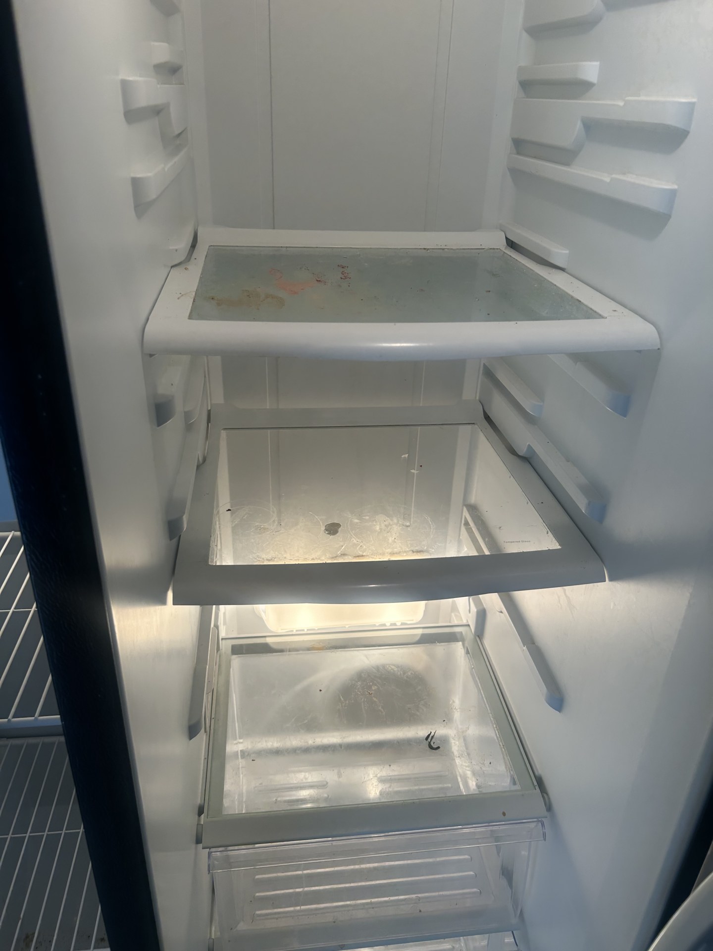 Refrigerator interior before cleaning with spills and crumbs on the shelves